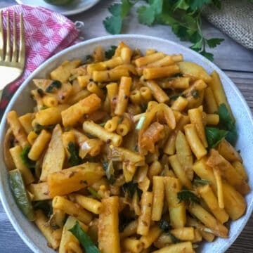 pasta with potatoes in curry sauce and sprinkled with fresh coriander served in a white bowl.
