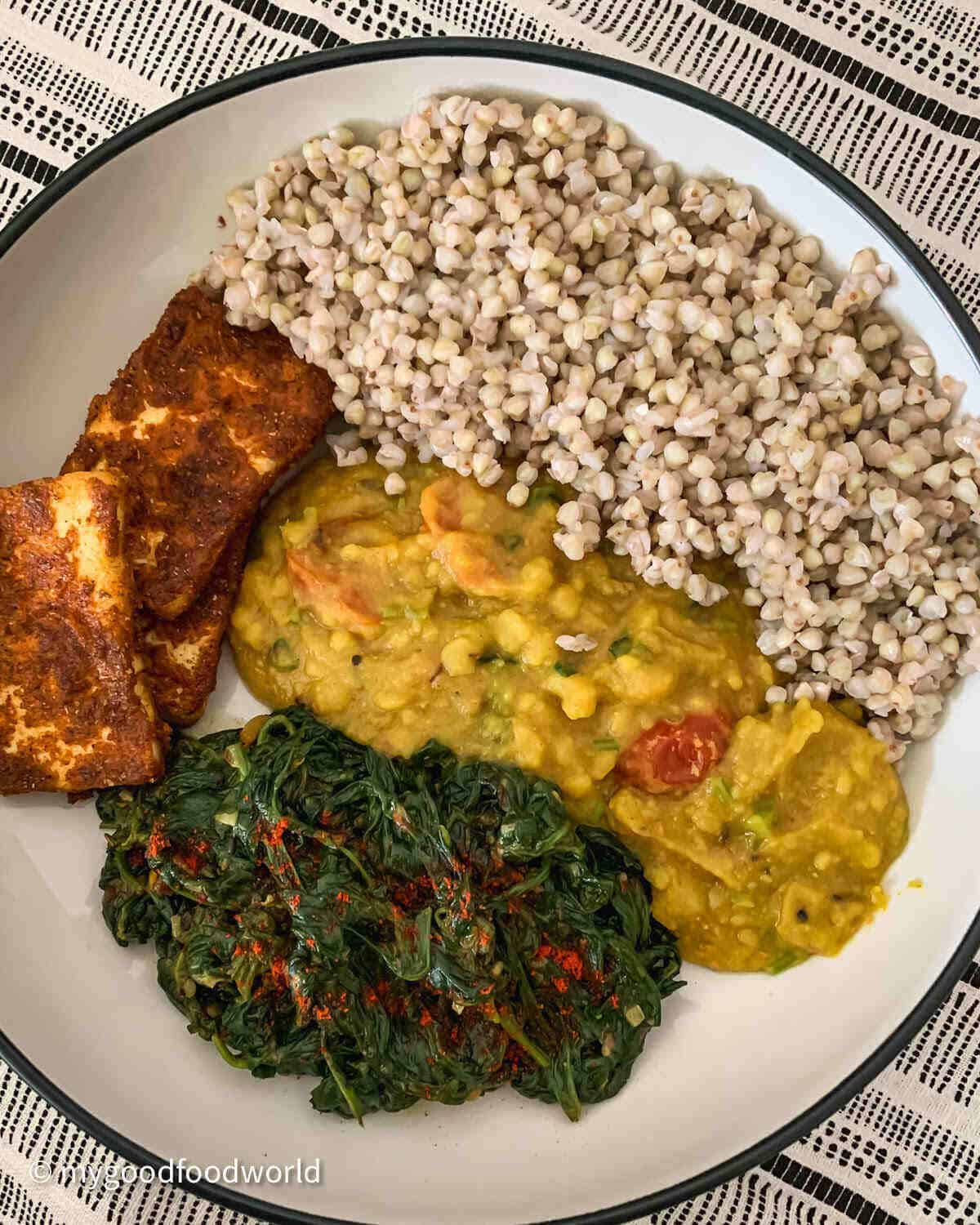 Cooked buckwheat groats served with lentils, greens and pan cooked paneer in a while bowl.