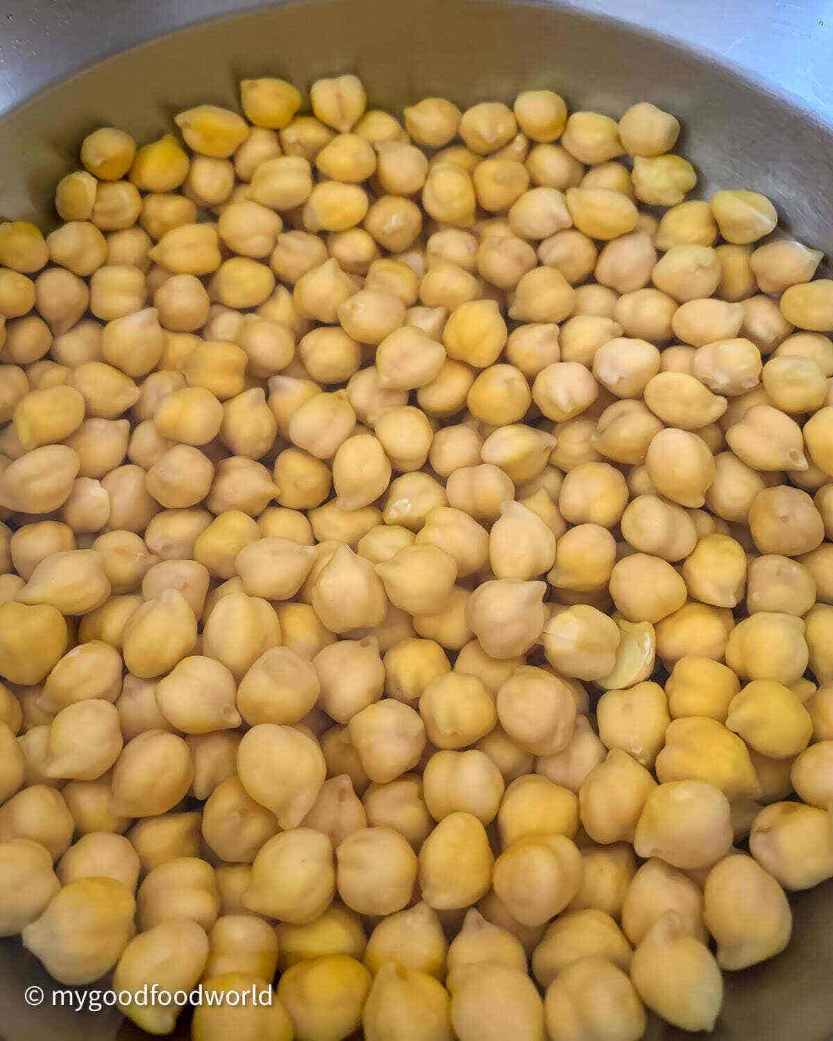 Garbanzo beans soaking in water in a wide bowl. This is a necessary step for making chickpea salad. 