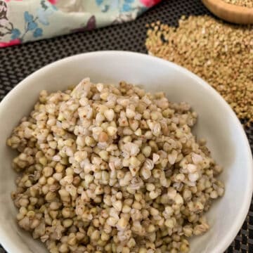 Cooked buckwheat groats served in a white bowl with a flower patten napkin and uncooked groats on the side.