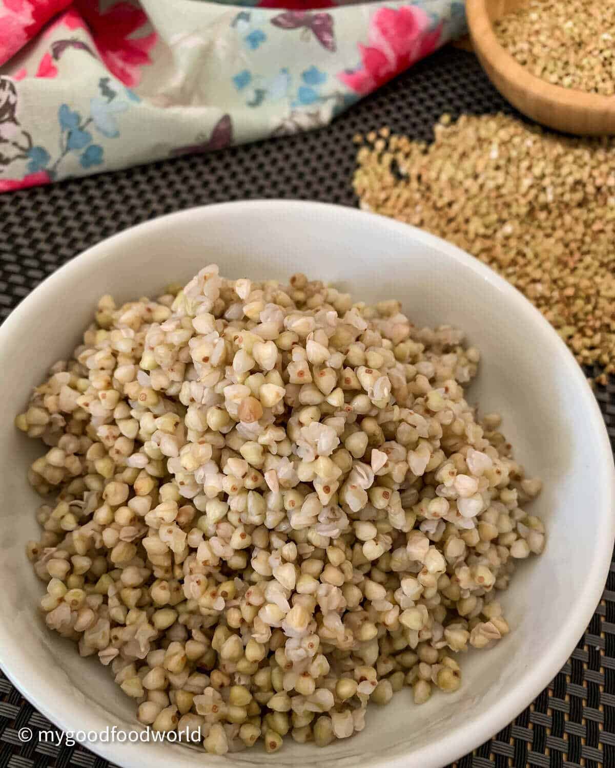 Cooked buckwheat groats served in a white bowl with a flower patten napkin and uncooked groats on the side.