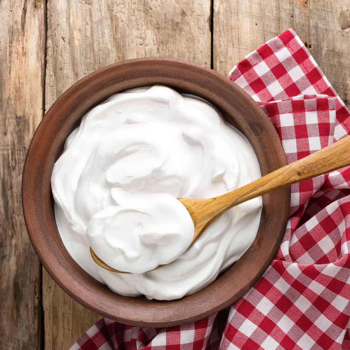 Plain curd / yogurt placed in an eartherware bowl and a wooden spoon scooping some of the curd.