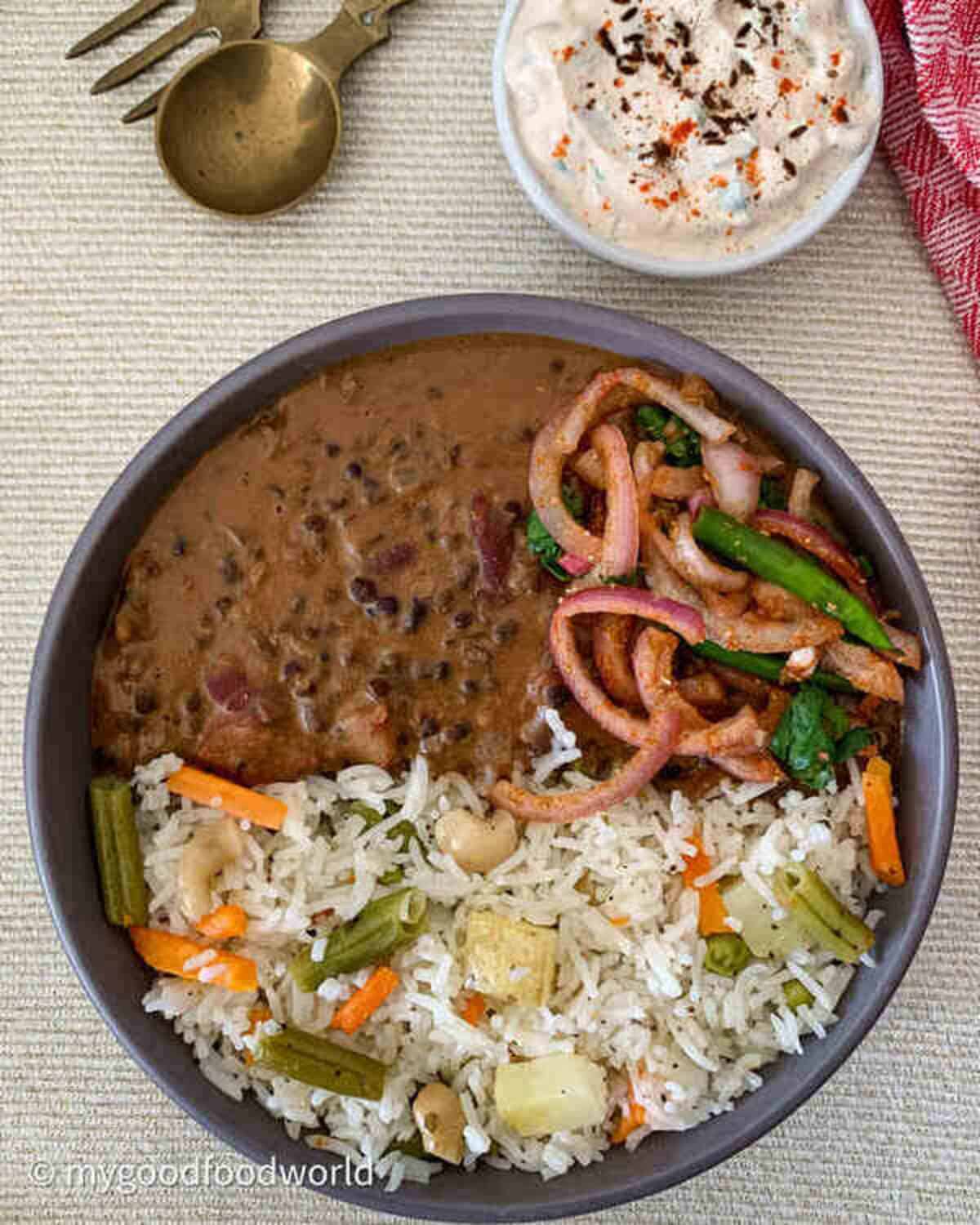 Vegetable pulao, dal makhani, lacha pyaz served in a round grey bowl with cucumber raita on the side.
