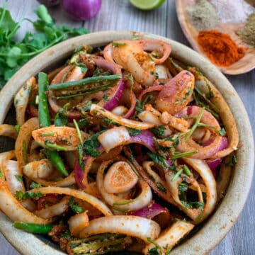 Spiced onions salad served in a rpund wooden bolw with raw onions, lemon wedge and spices placed on the side.