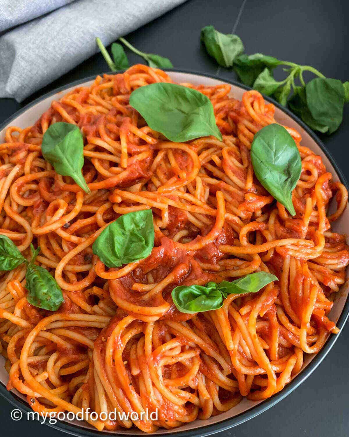 Spaghetti in tomato sauce served in a wide bowl with a black border and garnished with fresh basil leaves.