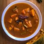Vegan stew served in a wide white bowl with a cut pumpkin and spices next to the bowl.
