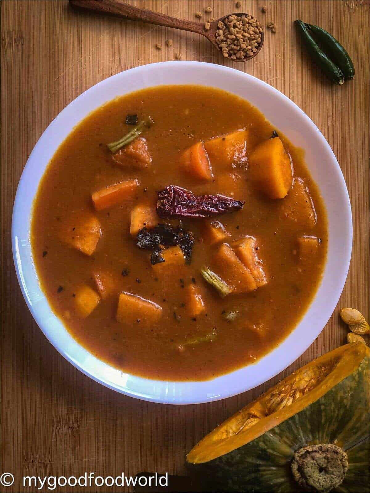 Vegan stew served in a wide white bowl with a cut pumpkin and spices next to the bowl.