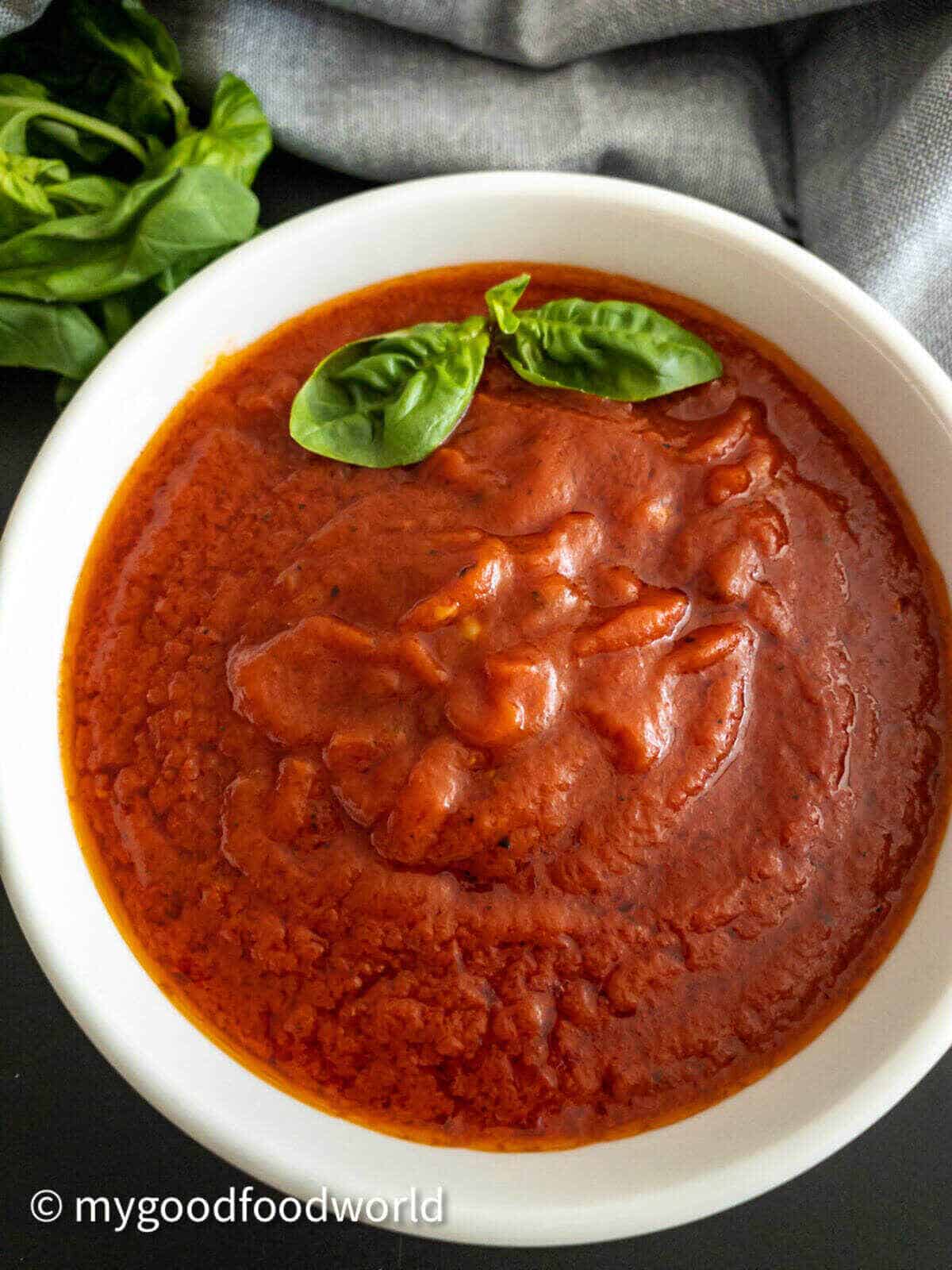 Hearty marinara sauce served in a white round bowl and garnished with two fresh basil leaves.
