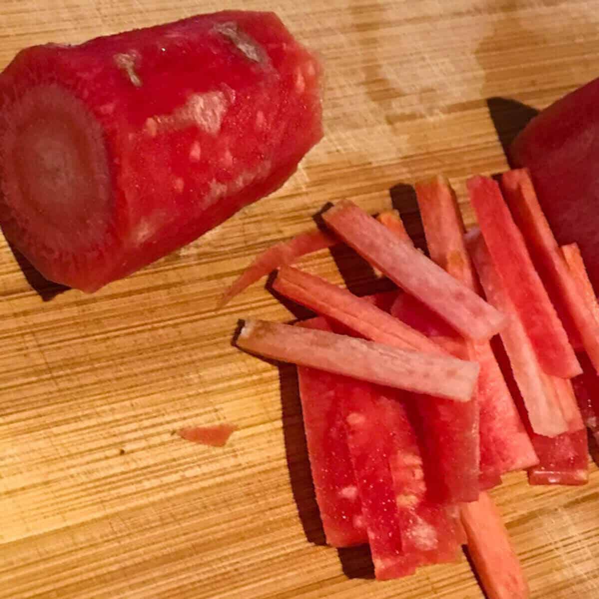 Red carrot cut into matchsticks and placed on a wooden board.