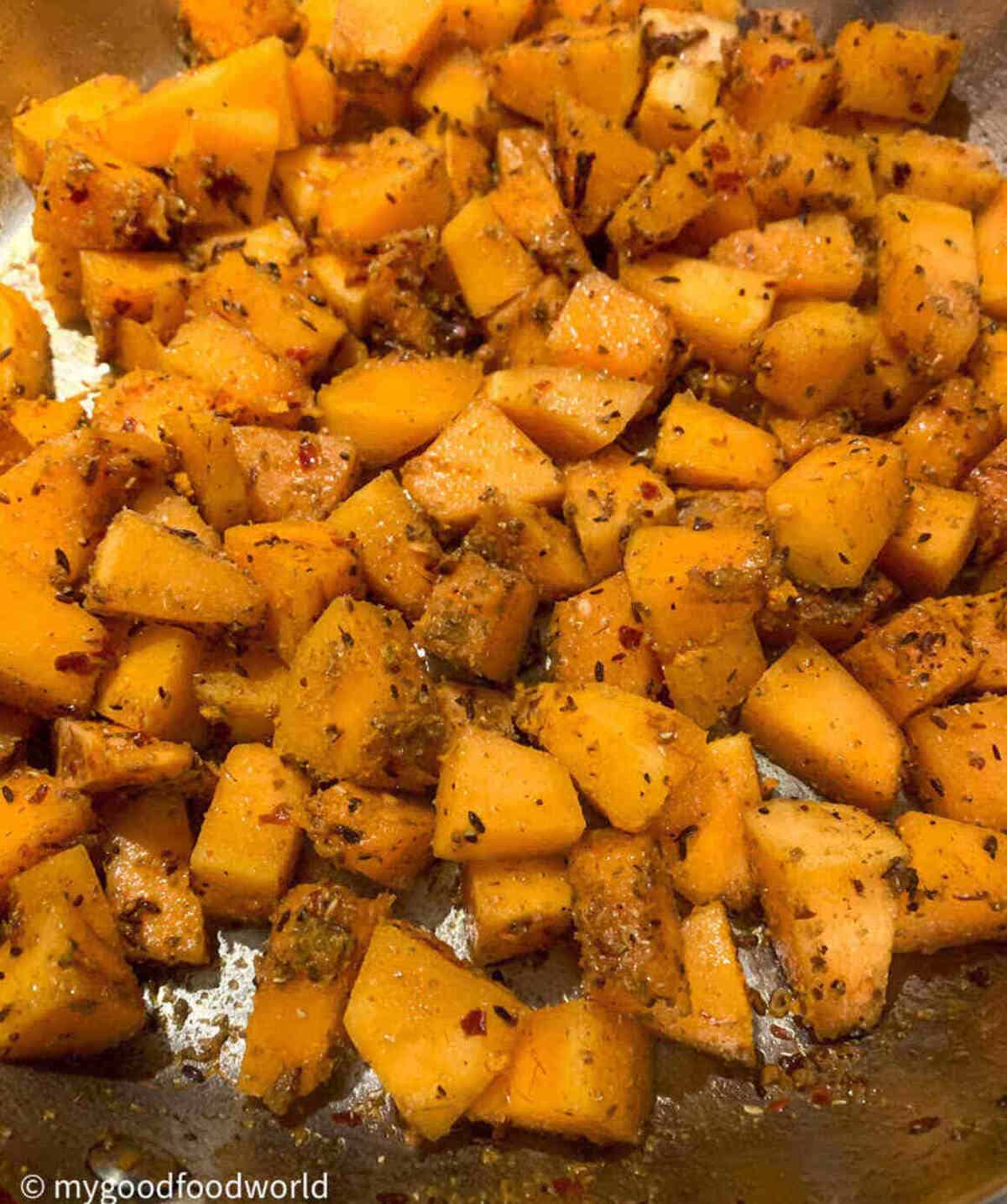Butternut squash cubes coated with spices sauteeing in a frying pan.