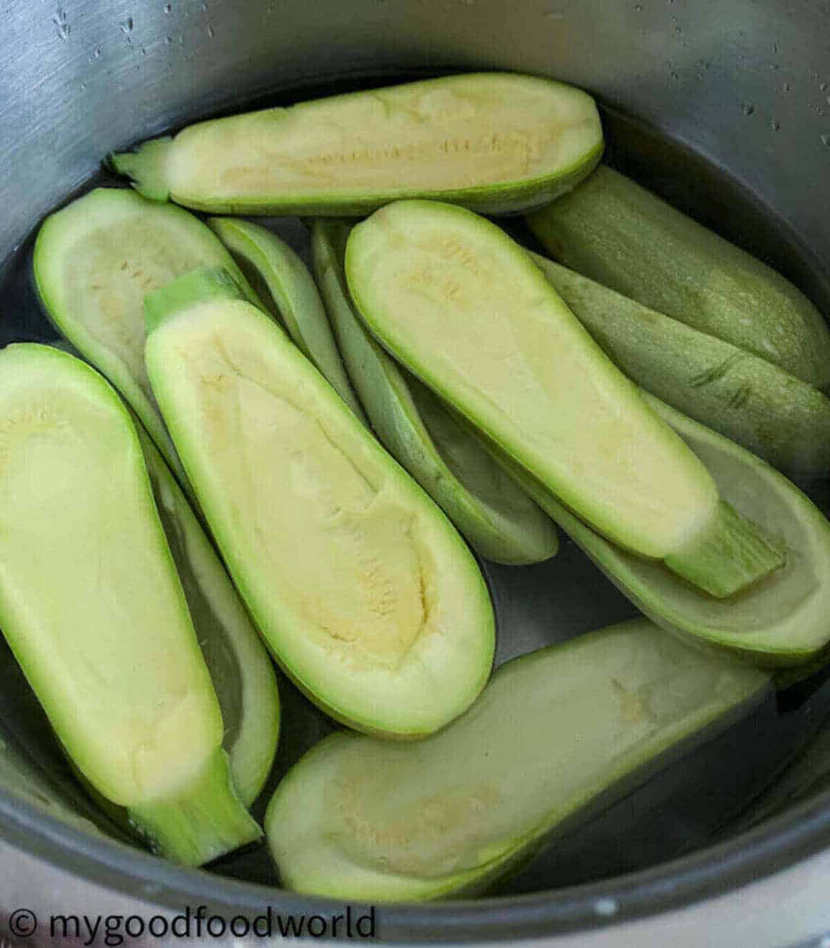 Many courgette halves, scooped and cleaned, placed in water.