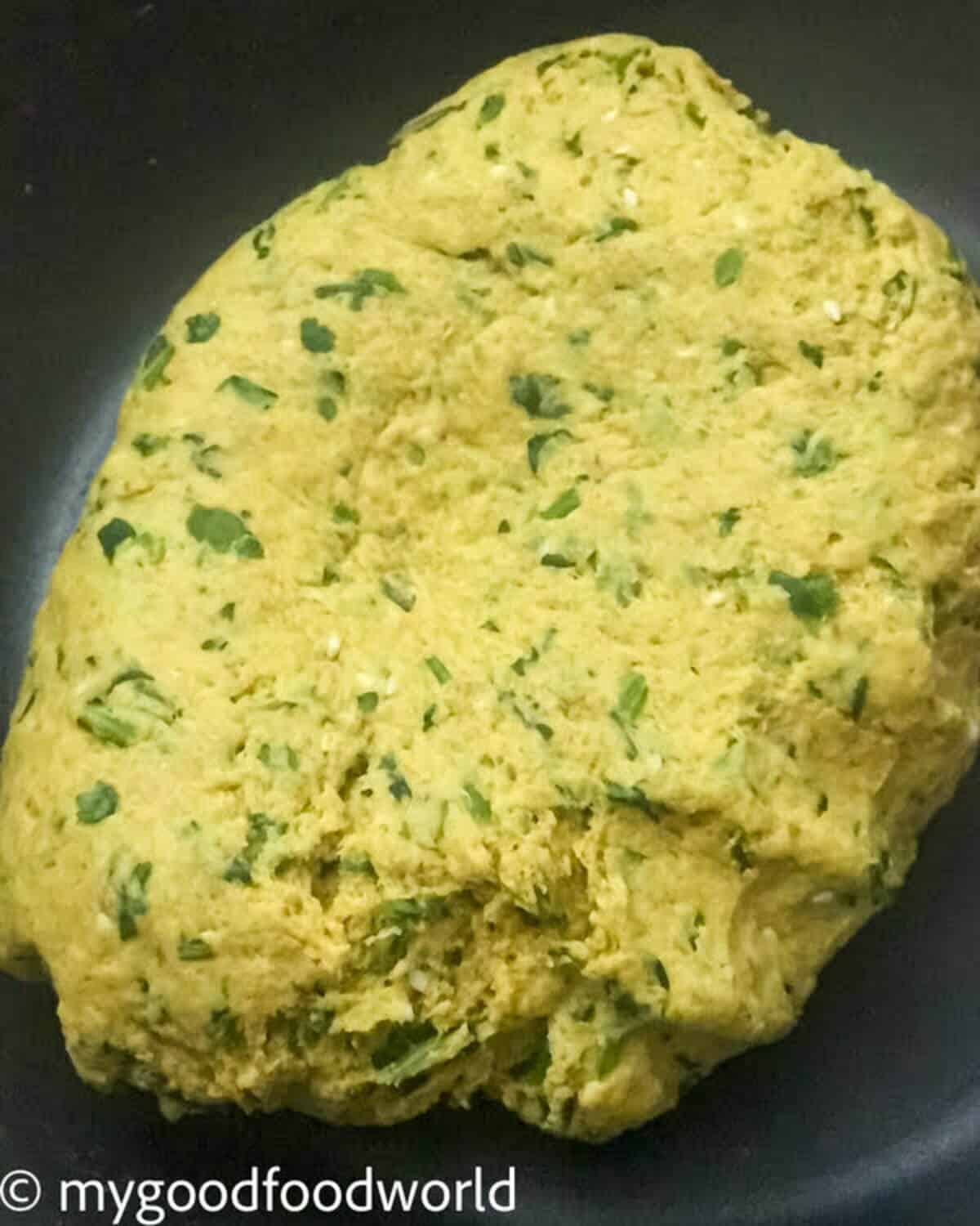 Yellow colored dough with specks of green cilantro and other spices placed in a bowl.