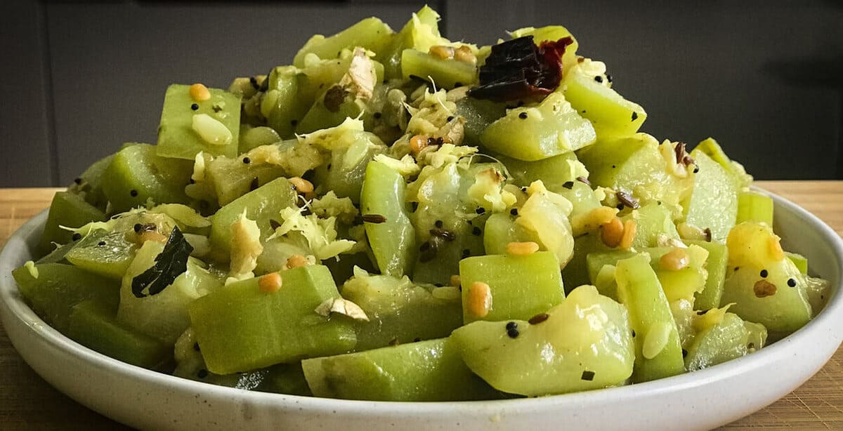 Sautéed bottle gourd recipe with spices such as cumin, mustard seeds and red chilli served on a white round plate.