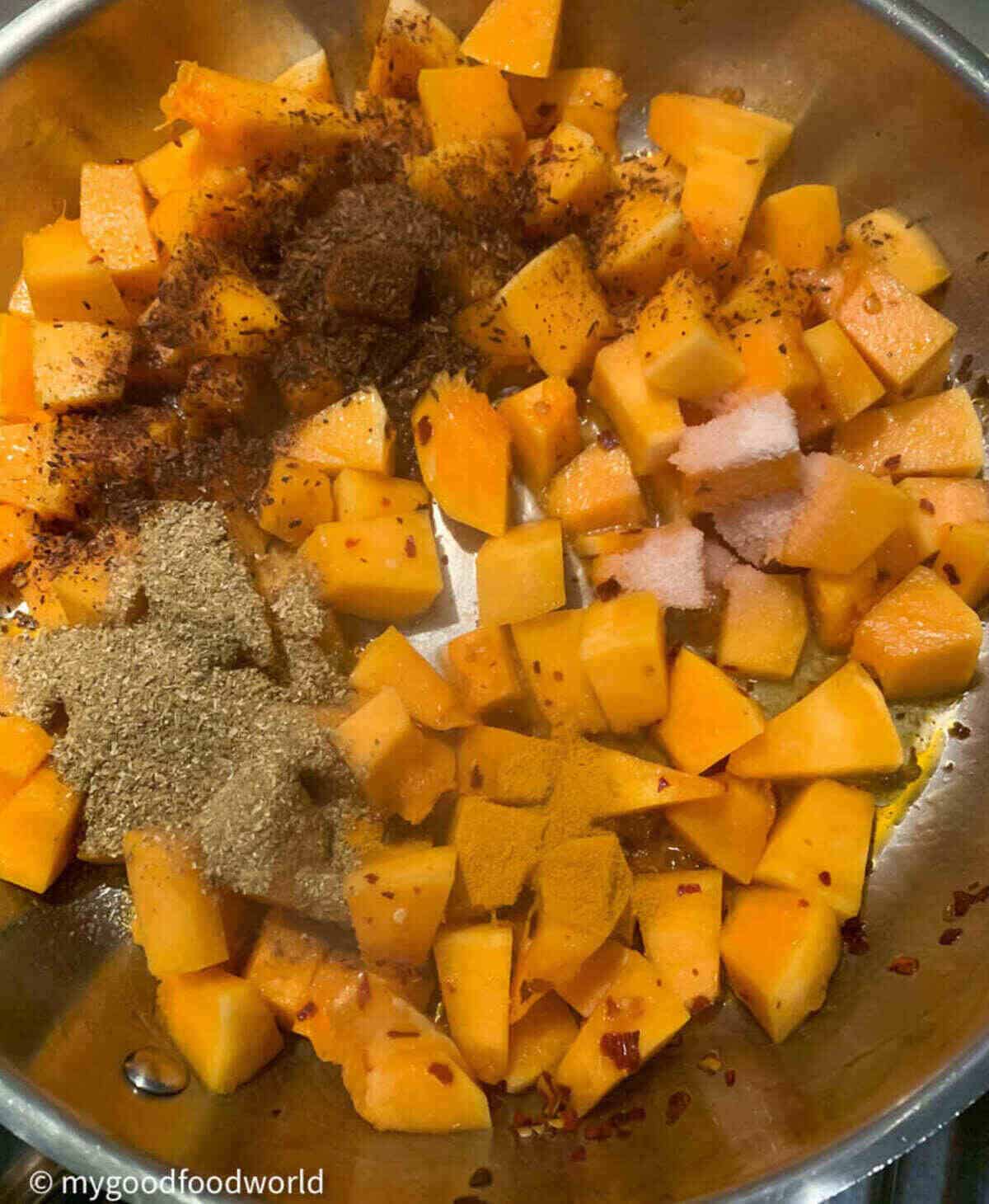 Spices on butternut squash cubes that are sautéing in a pan.