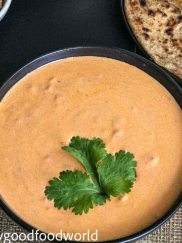 Creamy tomato raitha placed in a round black bowl with fresh coriander leaf garnish and placed on a cloth