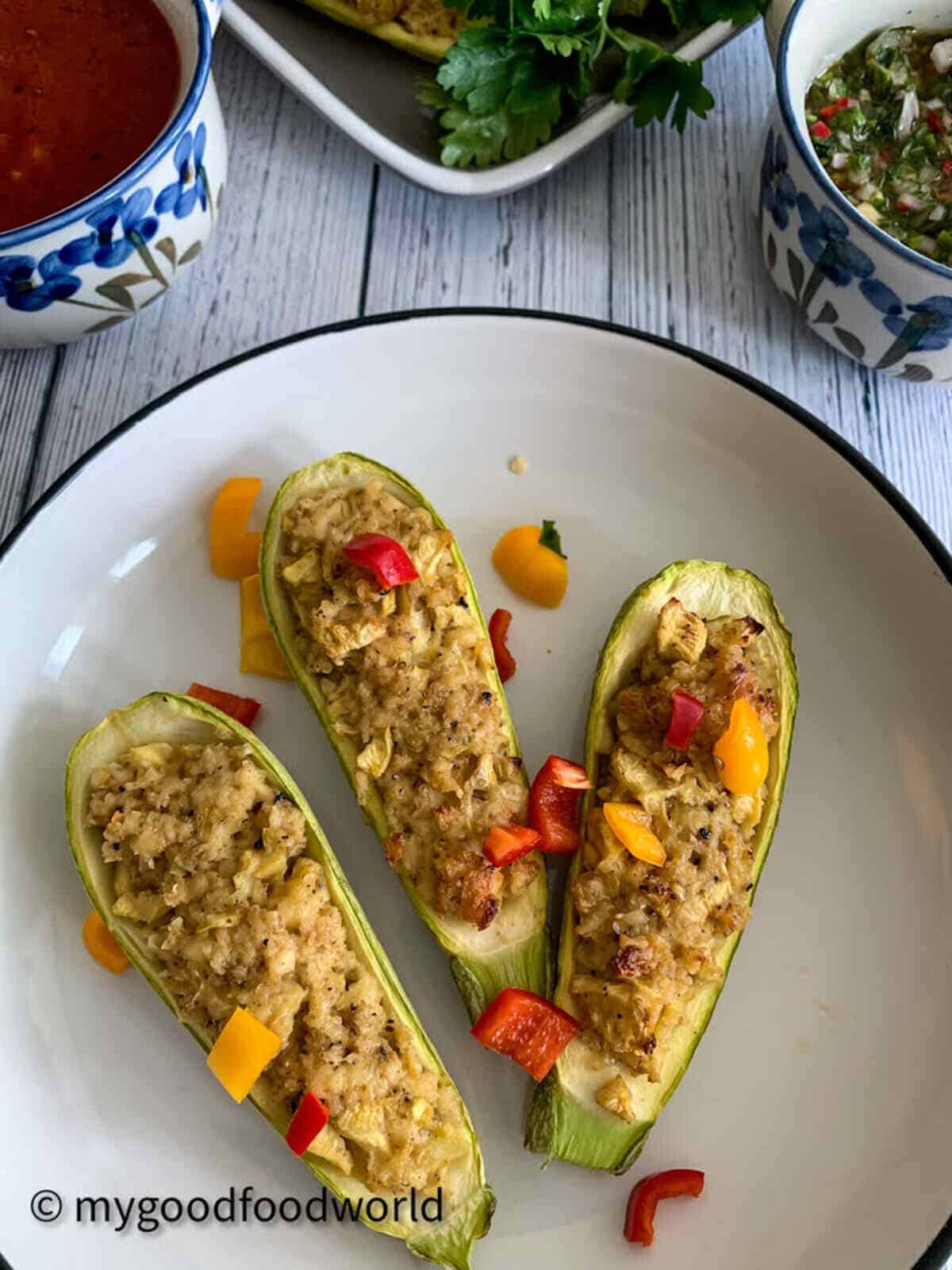 Three halves of baked zucchini boats vegetarian placed on a plate with cubed sweet peppers toppings.