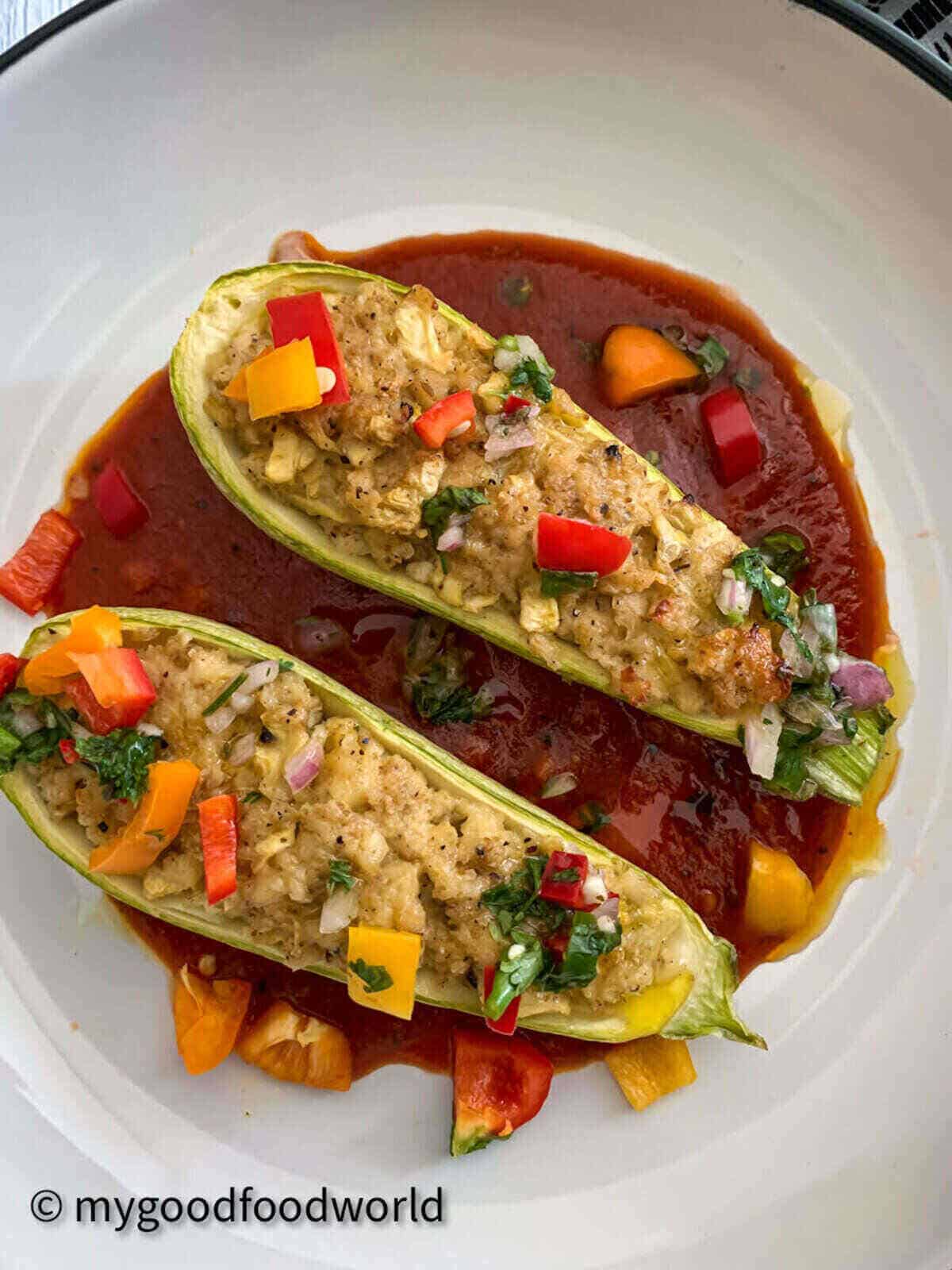 Vegetarian zucchini boats stuffed with scrambled paneer topped with cubes of colored peppers and placed on a bed of tomato sauce.
