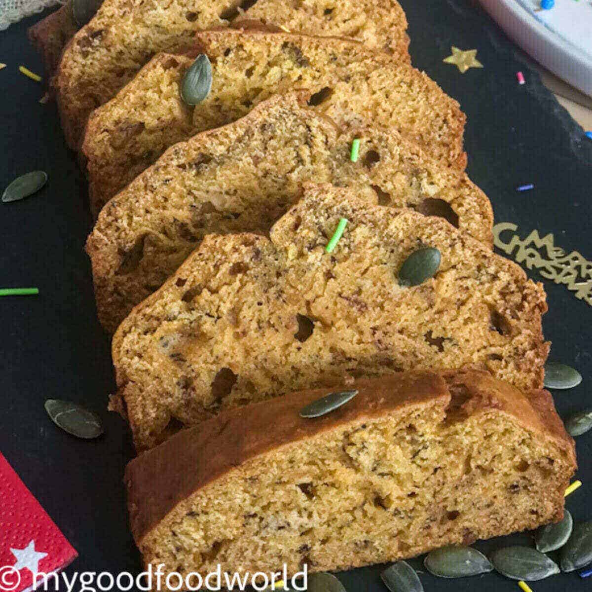 Slices of pumpkin banana bread placed on a black serving board with garnish of pumpkin seeds.