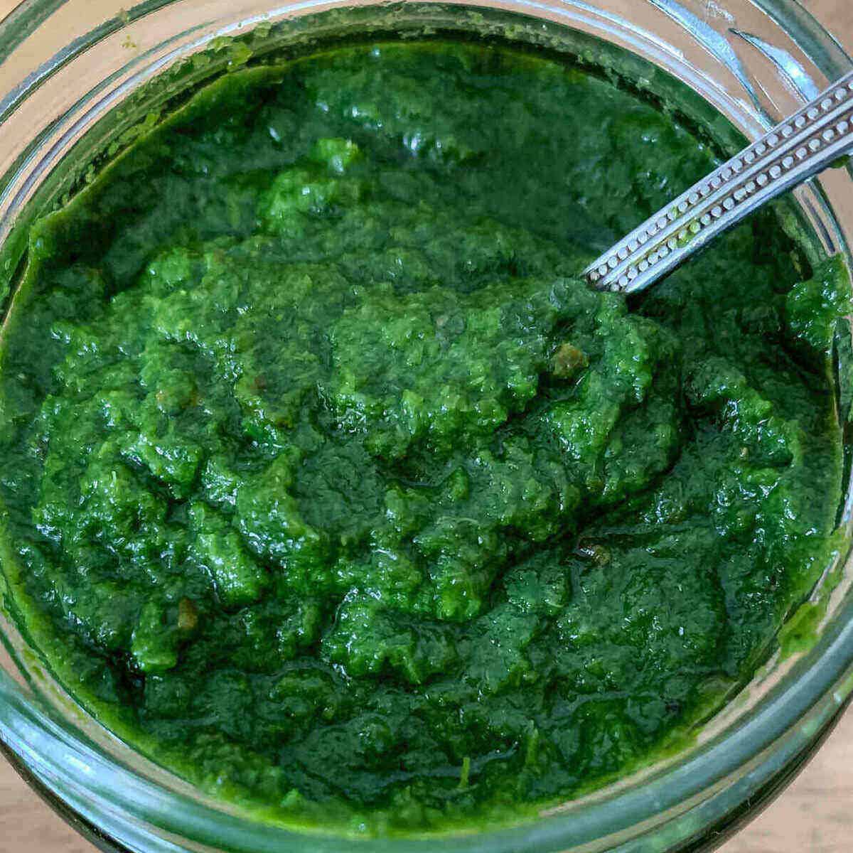 Cilantro mint chutney with amla gooseberry placed in a glass bottle and with a spoon placed in it for serving.