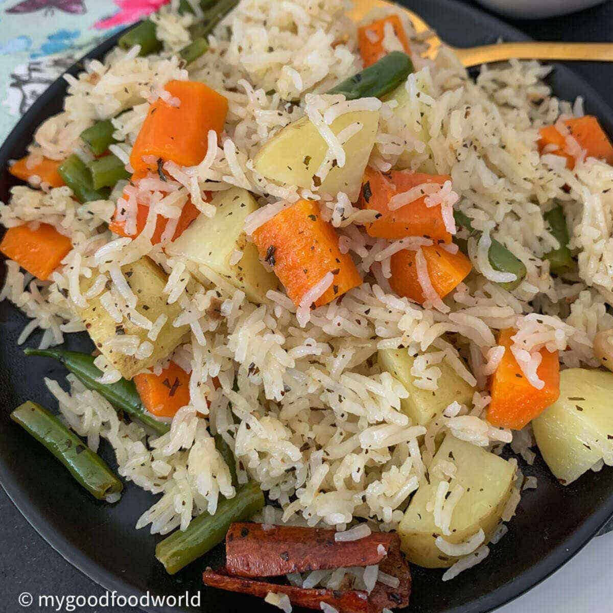 Veg pulao with carrot, beans and potatoes served in a black plate.