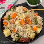 Vegetable pulao made with Basmati rice and vegetables is served on a plate with green chutney on the side.