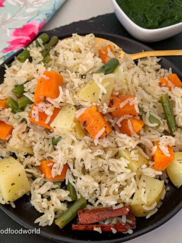 Vegetable pulao made with Basmati rice and vegetables is served on a plate with green chutney on the side.