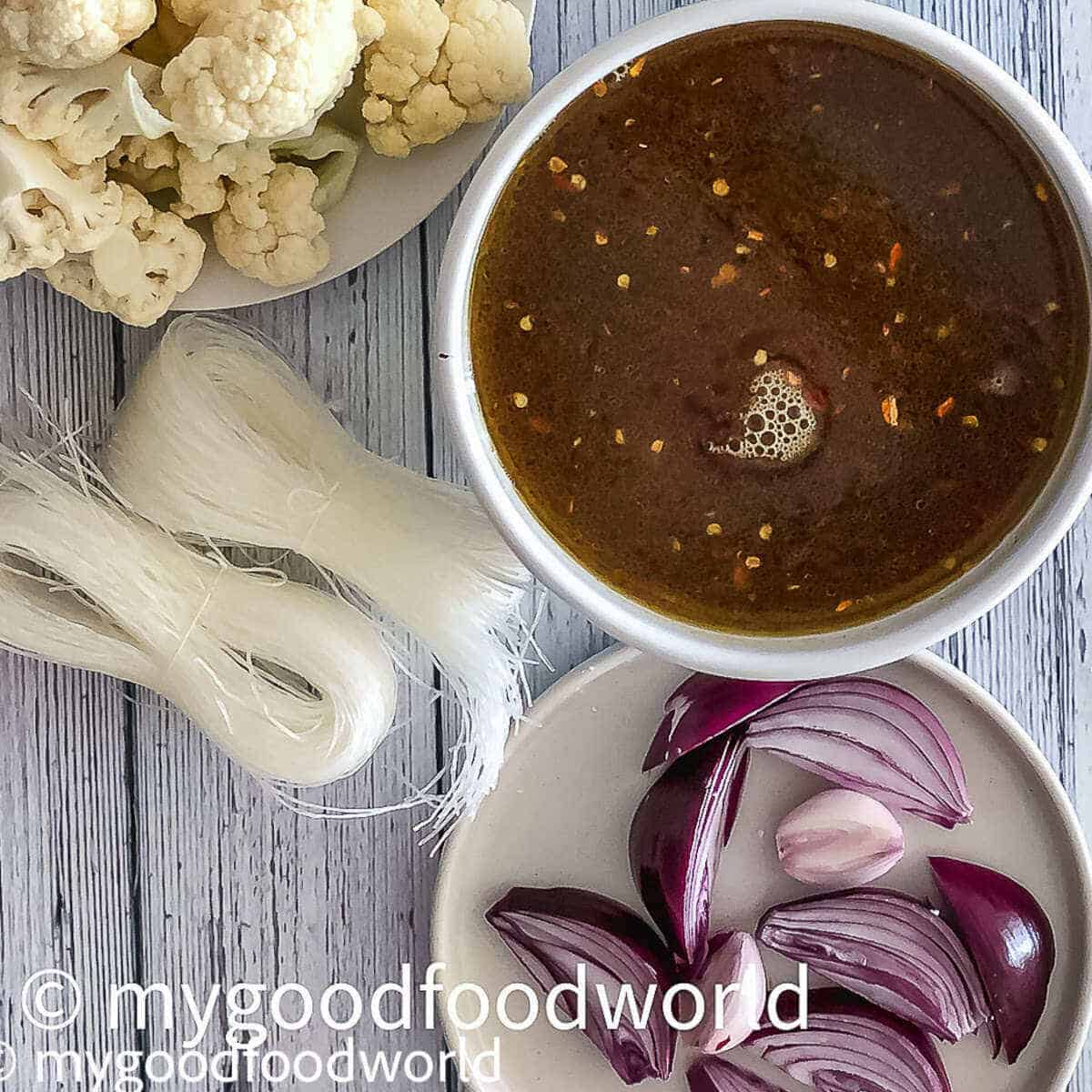 Spicy teriyaki broth placed in a white round bowl with cauliflower florets, onion wedges and glass noodles placed on the side.