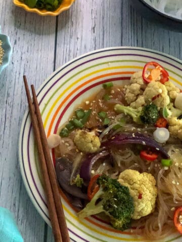 Vegan teriyaki noodles with veggies served in a plate with chopsticks rested on the plate.