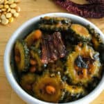 Bitter melon recipe dish served in a white bowl and with some chickpea lentils and dried red chilies on the side.