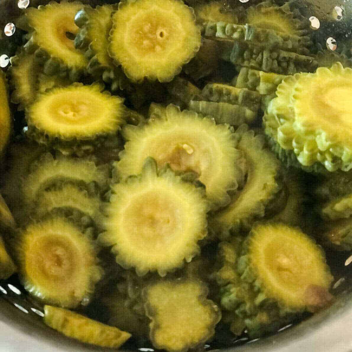 Boiled bitter melon slices placed in a sieved colander.