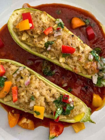 Vegetarian zucchini boats with crumbled paneer served on a bed of tomato sauce and with herbed salsa garnish.
