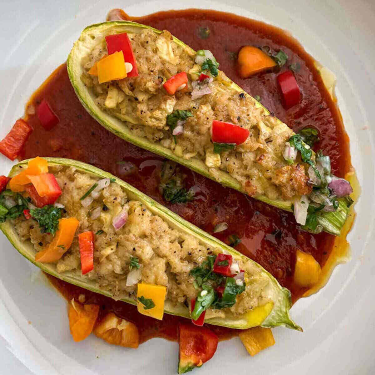 Vegetarian zucchini boats stuffed with crumbled paneer served on a bed of tomato sauce and with herbed salsa garnish.