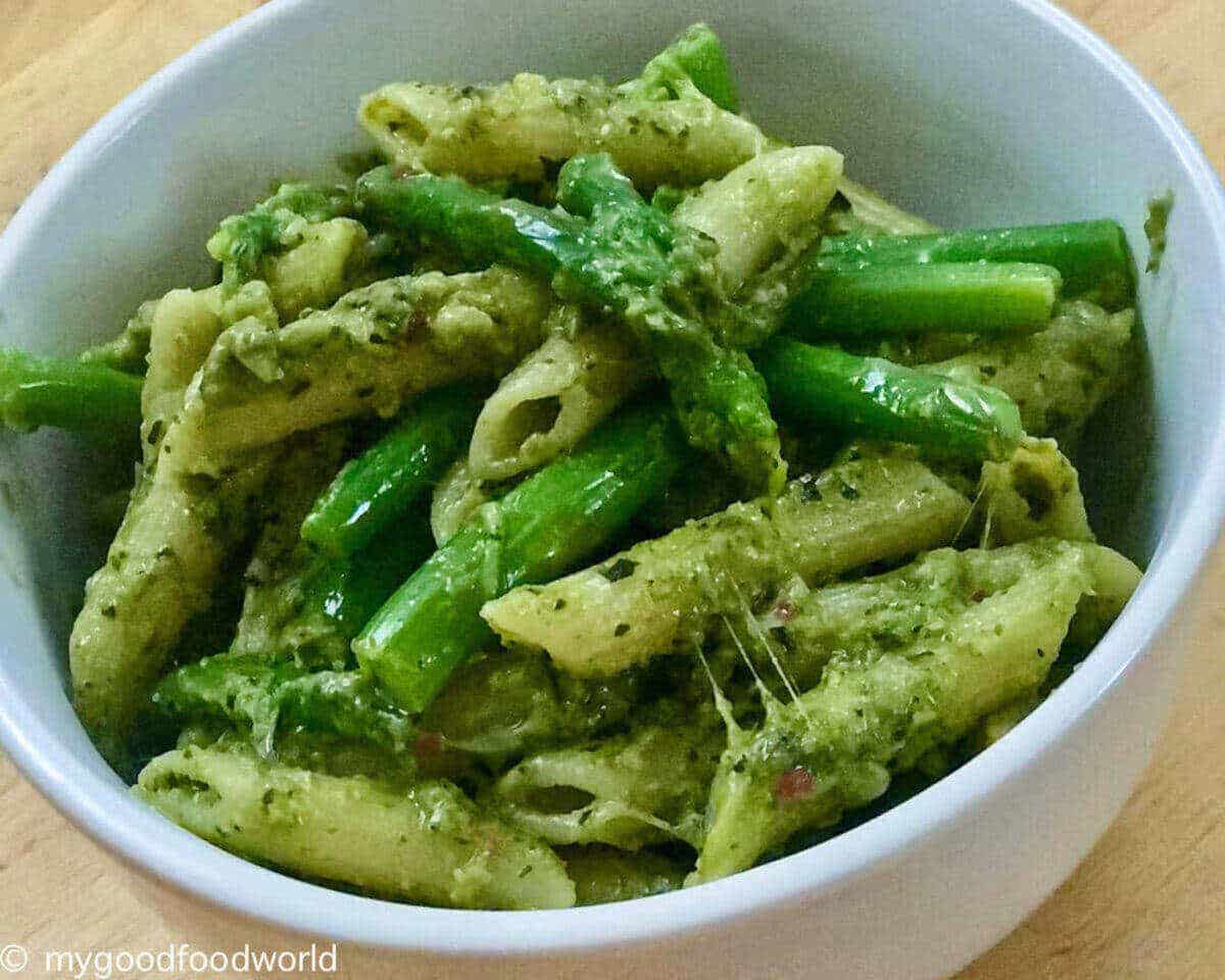 Bright green colored basil pesto past with tender stem broccoli and cheese served in a round white bowl.