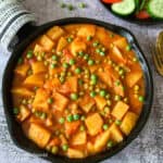 Aloo matar recipe served in a black round pan with some salad on the side.