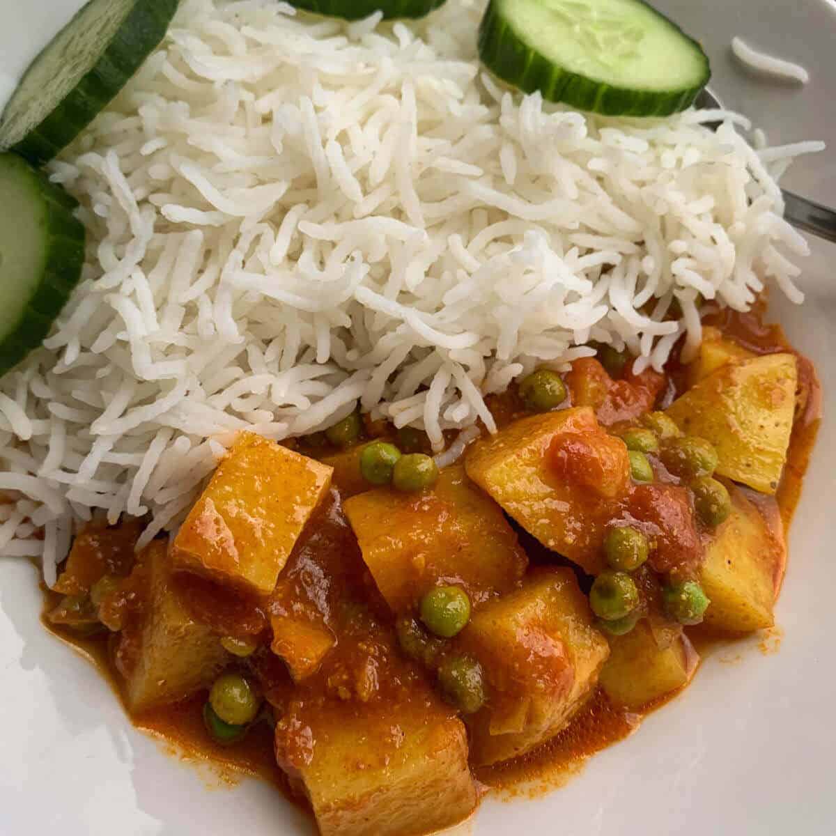 Alu matar curry served with white basmati and some cucumbers rounds on the side.