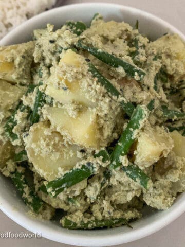 Creamy green beans and potatoes in poppy seeds sauce placed in a round white bowl.