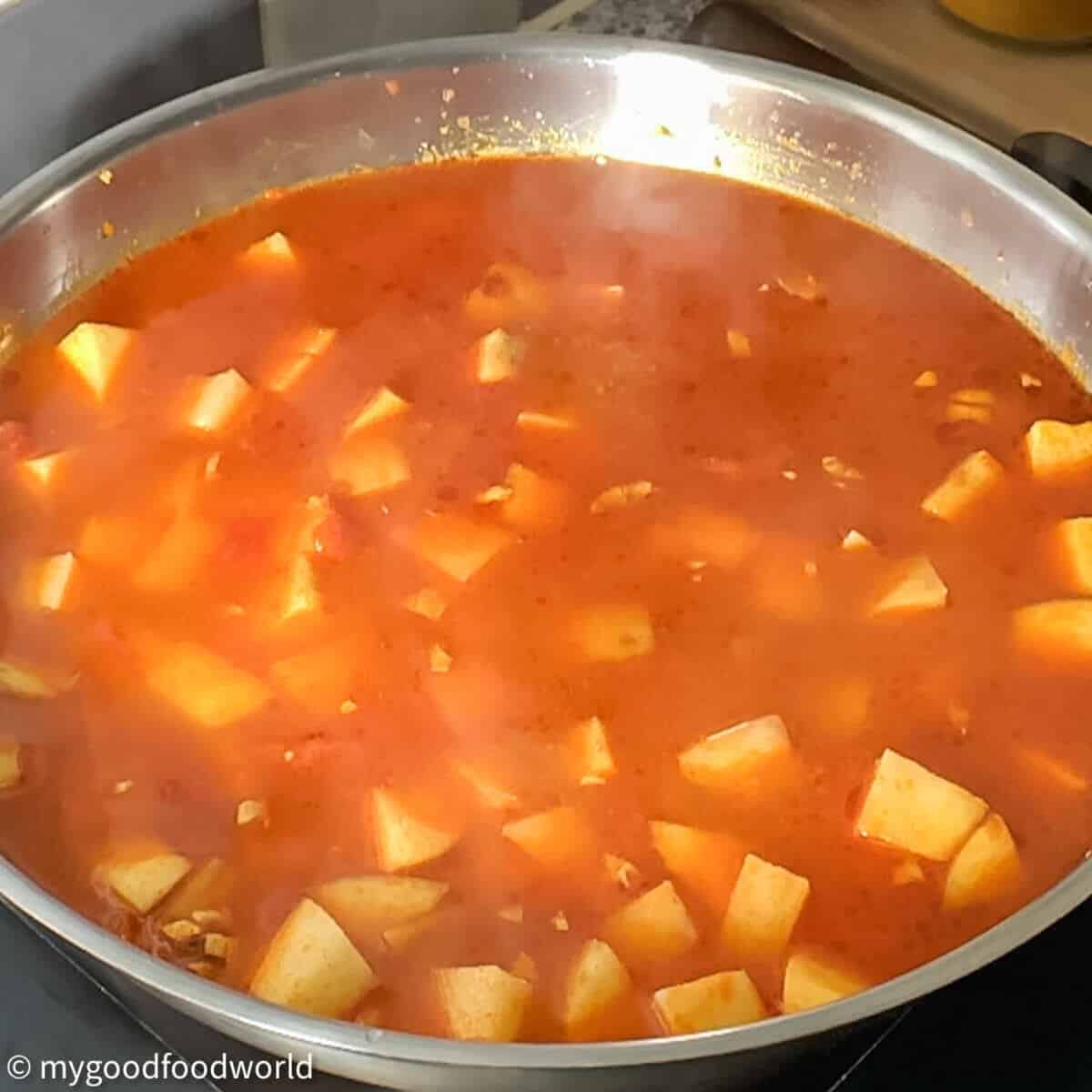 Potatoes cooking in spices and gravy in a stainless steel frying pan.