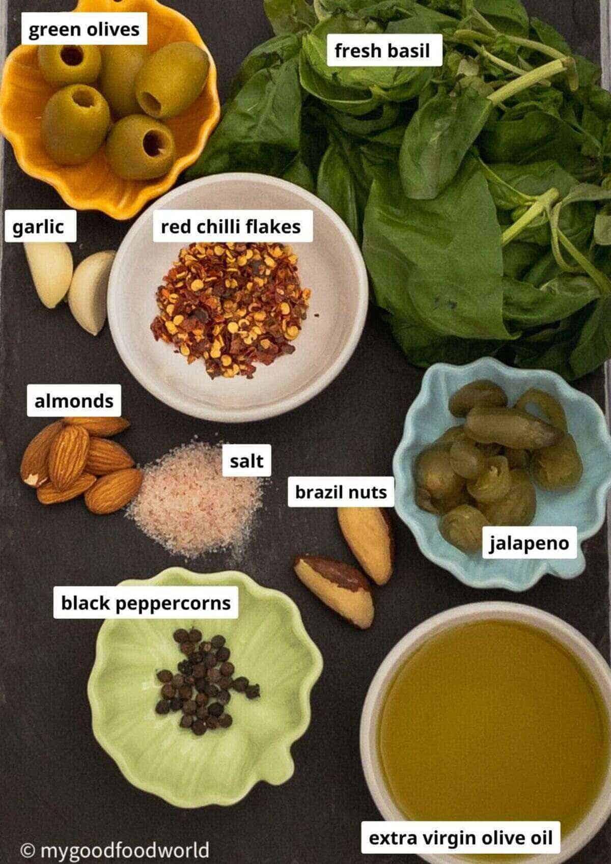 Recipe ingredients for vegan pesto are placed in small bowls on a black background.