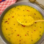 Lemony yellow lentil soup served in a round grey soup with a golden colored spoon scooping out some of the soup.