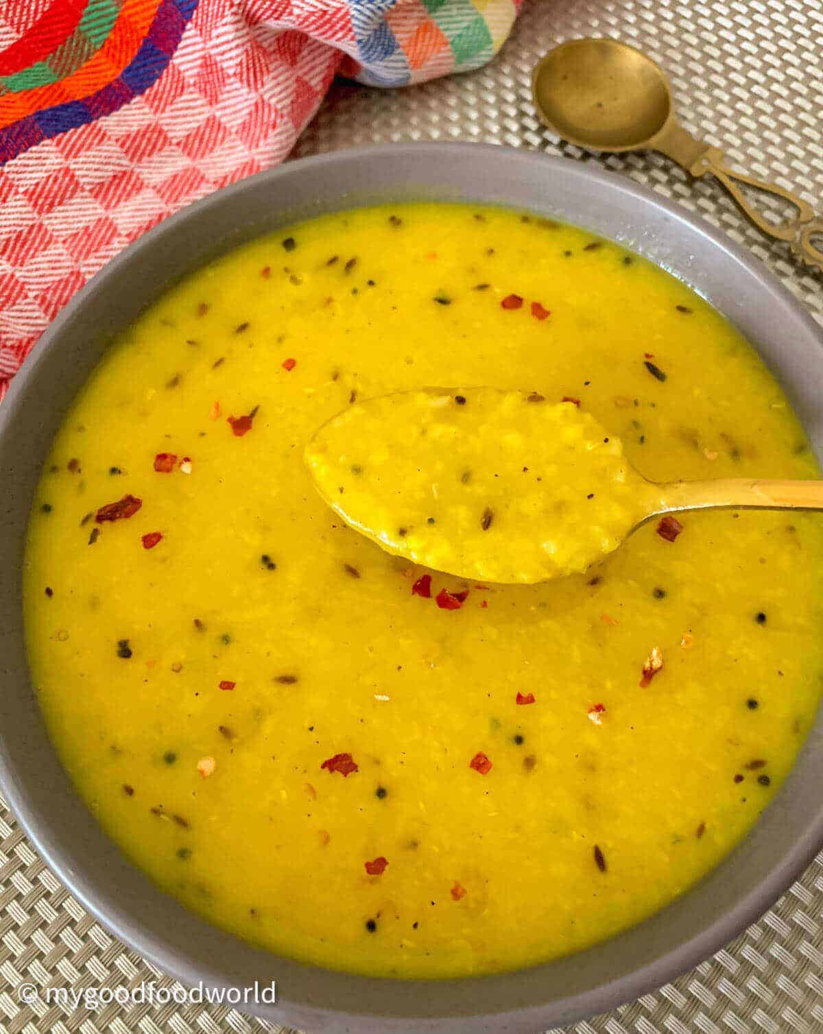 Moong dal soup is served in a round grey soup with a golden colored spoon scooping out some of the soup.
