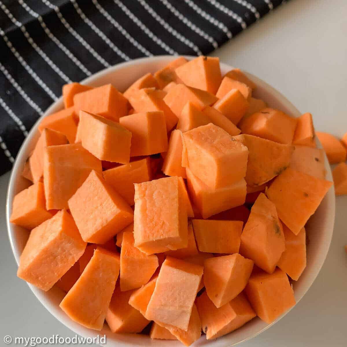 Sweet potatoe chopped and placed in a white bowl. A black cloth with white stripes is placed on the side of the bowl.