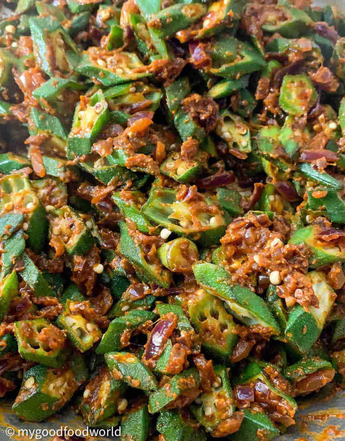 Close up shot of sliced bhindi pieces frying in masala paste that is thickly coating the bhindi.