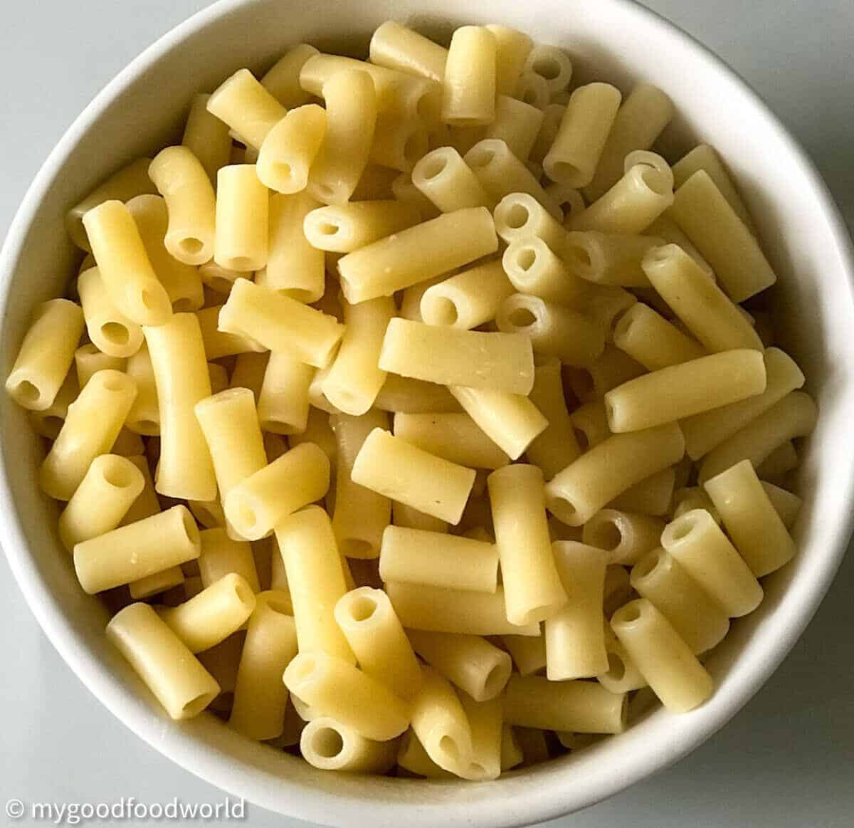 Boiled tube-shaped macaroni plced in a round shaped white bowl. The bowl is placed on a light colored background.