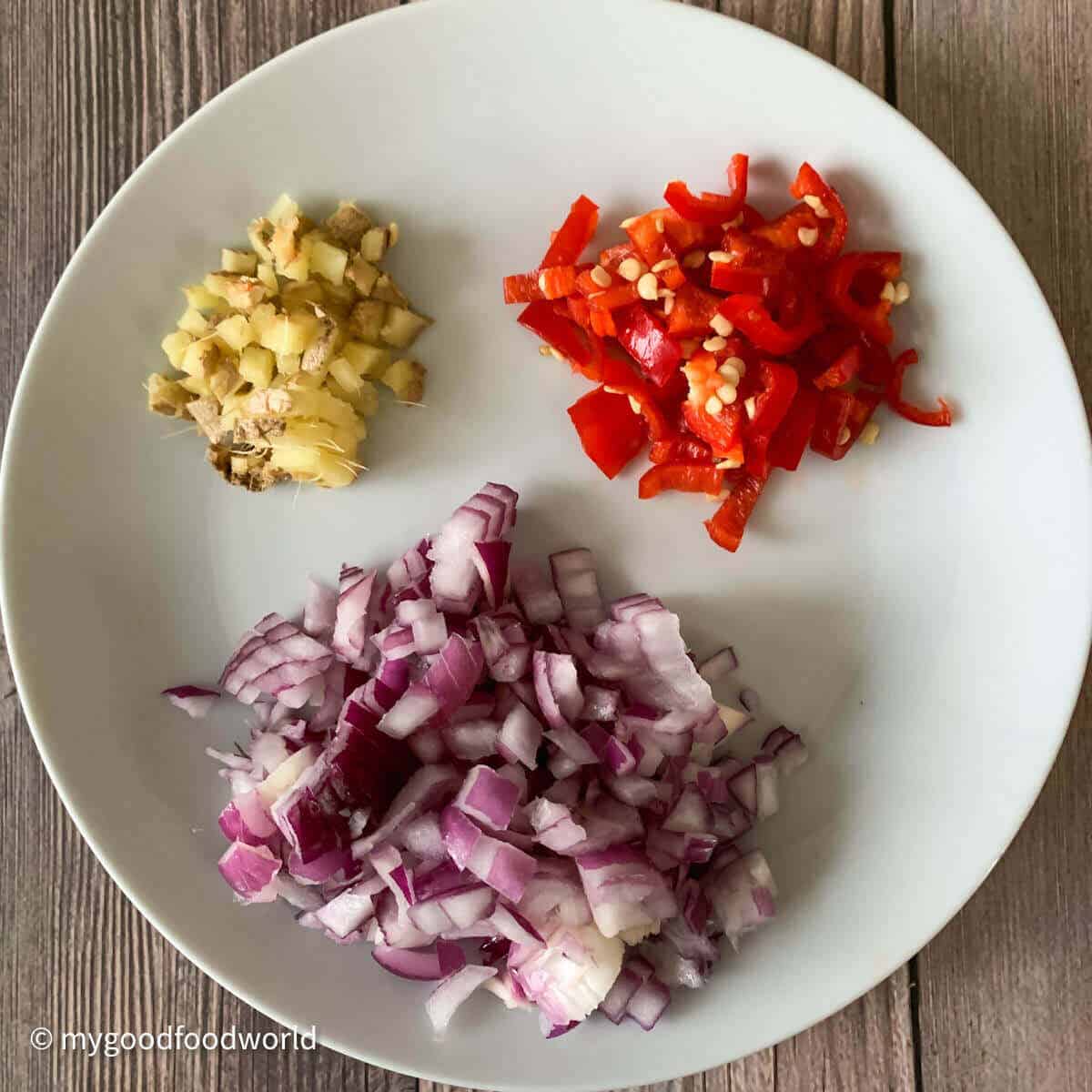 Finely chopped onions, fresh red chili and ginger placed in a round white plate on a dark brown background.