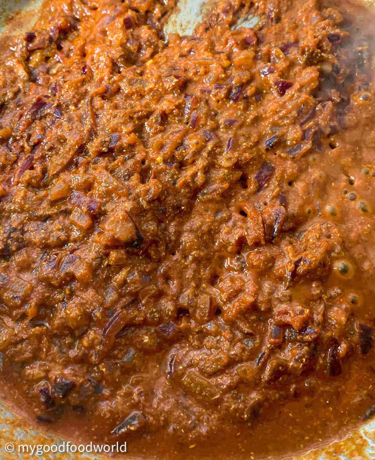 Masala paste with ginger garlic paste, spices and tomato paste in it, cooking in a saucepan.