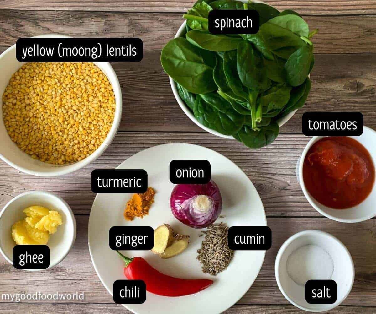 Ingredients for spinach dal displayed in round bowls and plates and placed on a dark brown textured background.