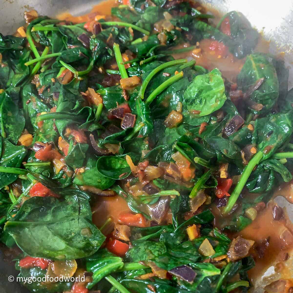 Spinach wilting and cooking in tomato gravy.