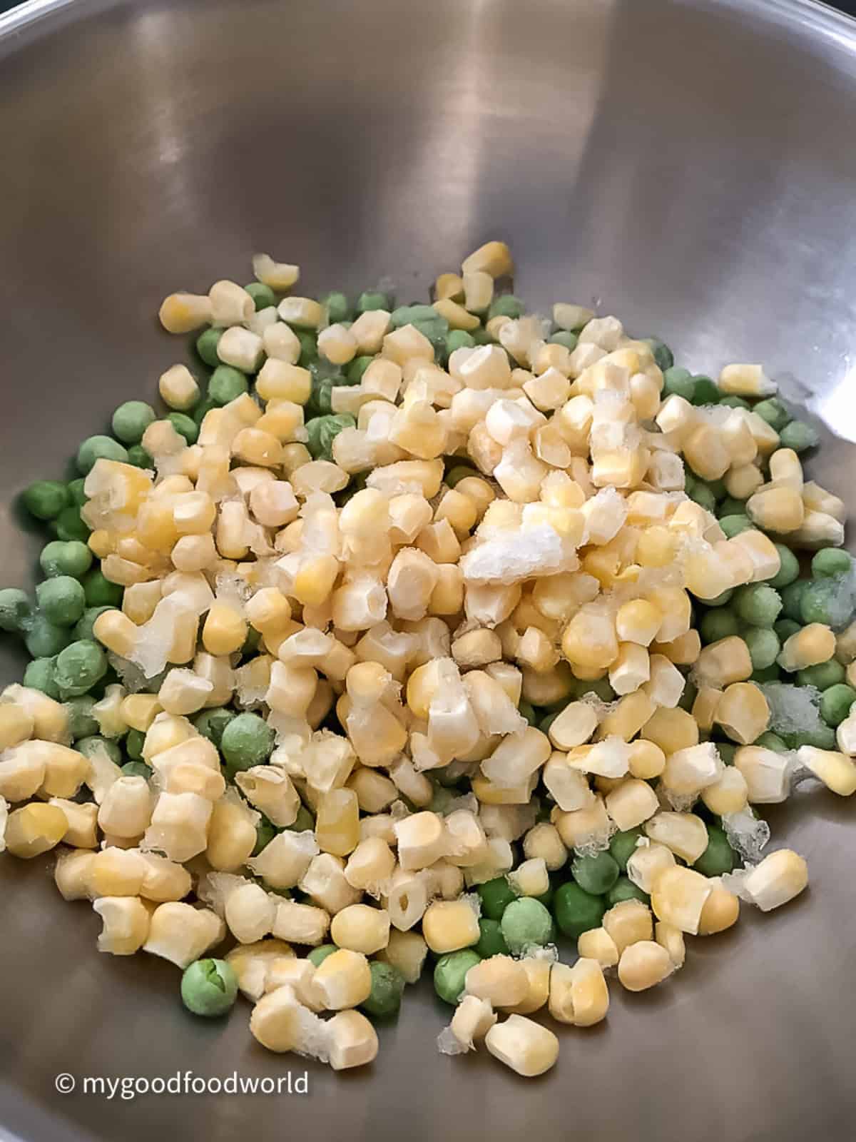 Frozen petit pois and frozen sweetcorn placed in a stainless steel wok for cooking.