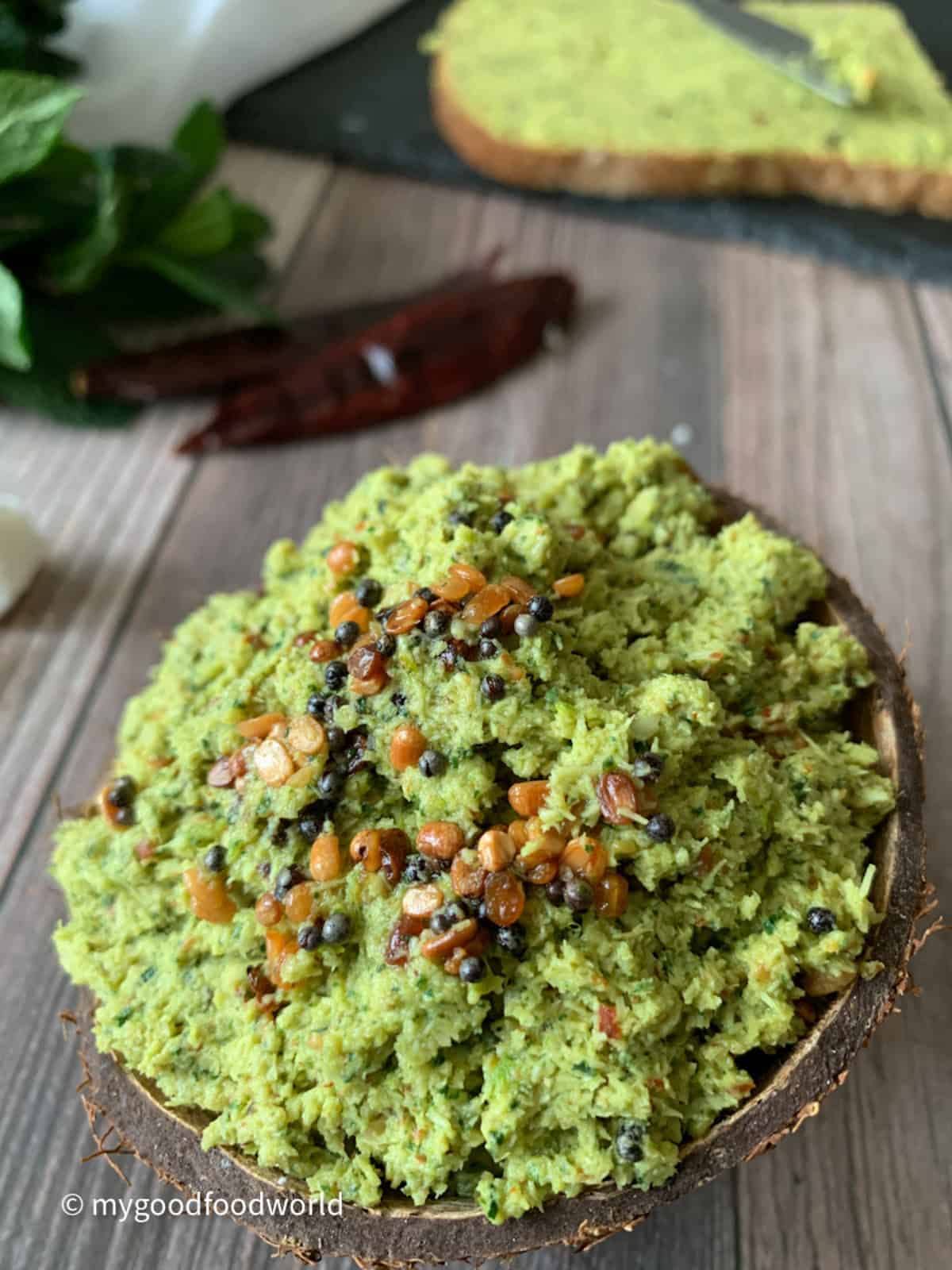Green colored chutney made with coconut and mint leaves placed in a coconut shell.
