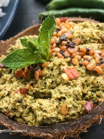 Homemade mint and coconut chutney with tempering of fried lentils placed in a coconut shell. A spring of fresh mint is placed on the chutney.